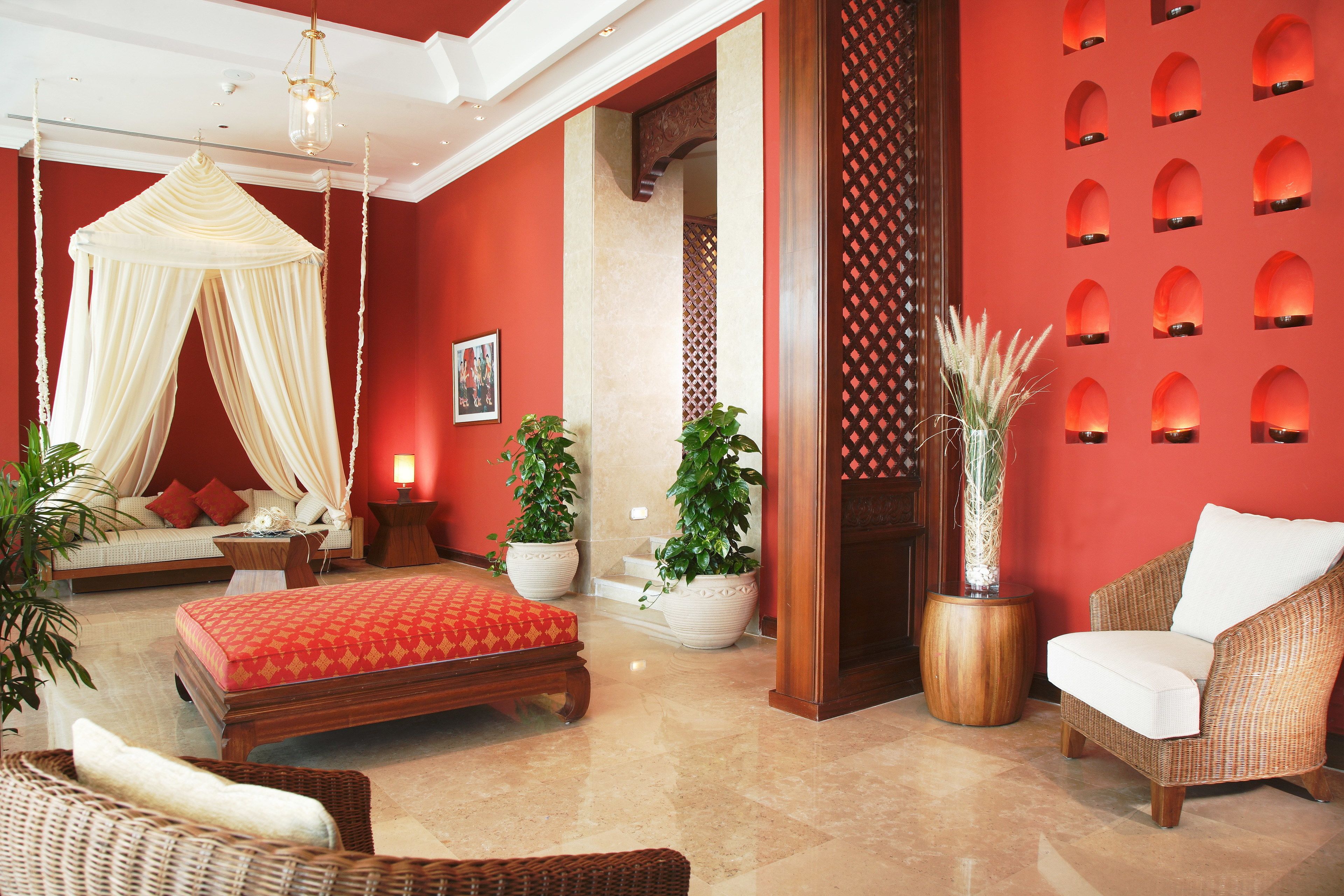 A room with a bed, a sitting area with a chair, a small table, and potted plants.