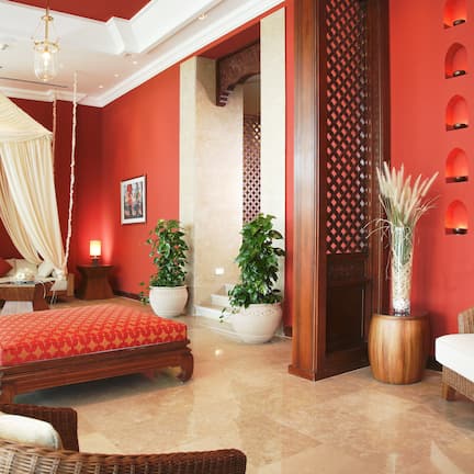 A room with a bed, a sitting area with a chair, a small table, and potted plants.