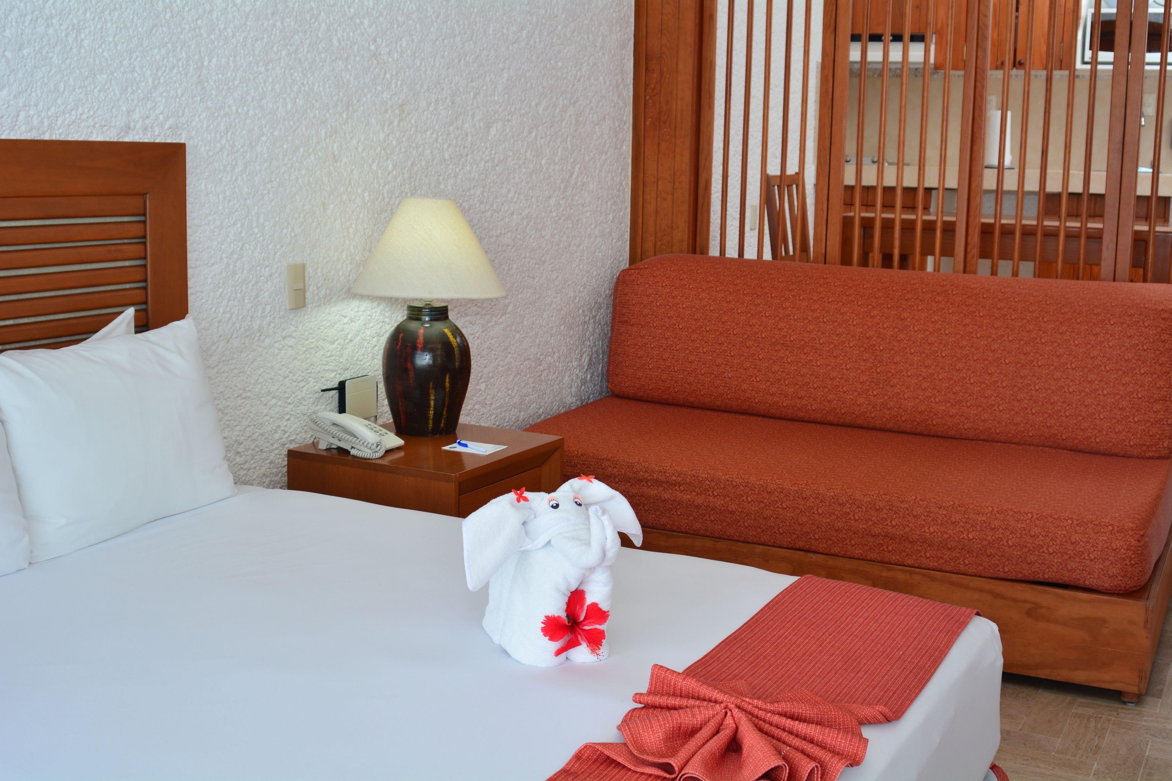 Habitación de hotel con cama, mesita de noche con lámpara, teléfono y sofá rojo.