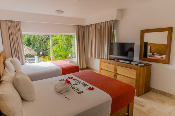 Habitación de hotel con dos camas, televisión, cómoda de madera y ventana grande con vistas a zonas verdes.
