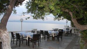 An outdoor dining area with tables and chairs, overlooking a body of water. - Hotel Pappas (Loutraki-Agioi Theodoroi)