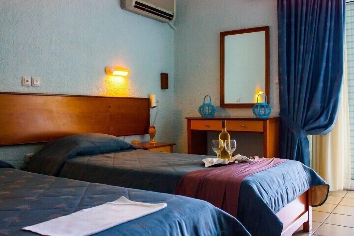 Hotellihuone, jossa on kaksi sänkyä, yöpöytä, peili ja ikkuna, jossa on verhot.