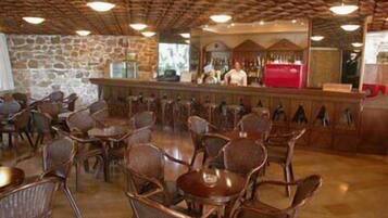 Restaurante com parede de pedra, teto de madeira e área de bar com balcão vermelho.
