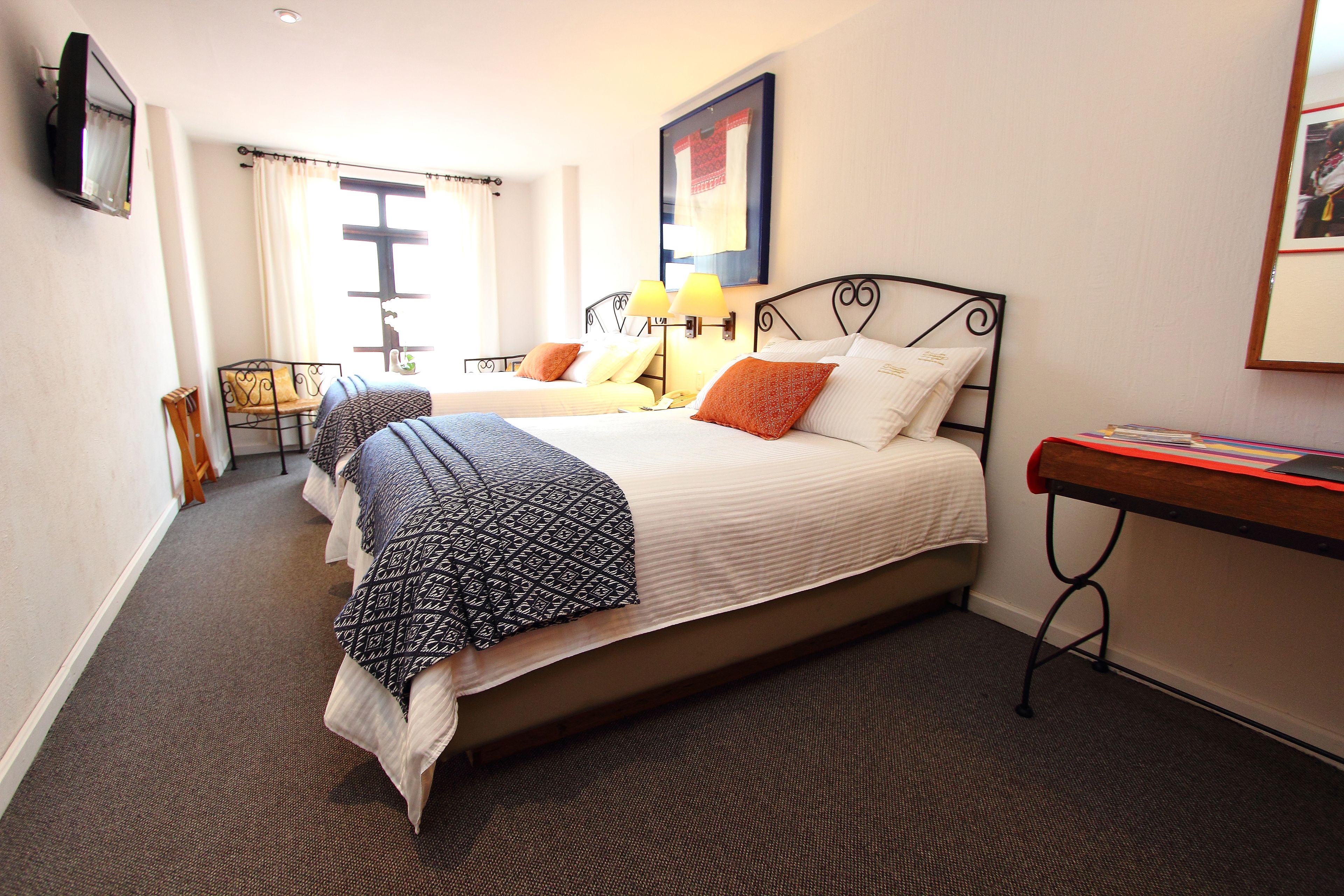 A hotel room with two beds, a desk, a chair, a TV, and a window with curtains.