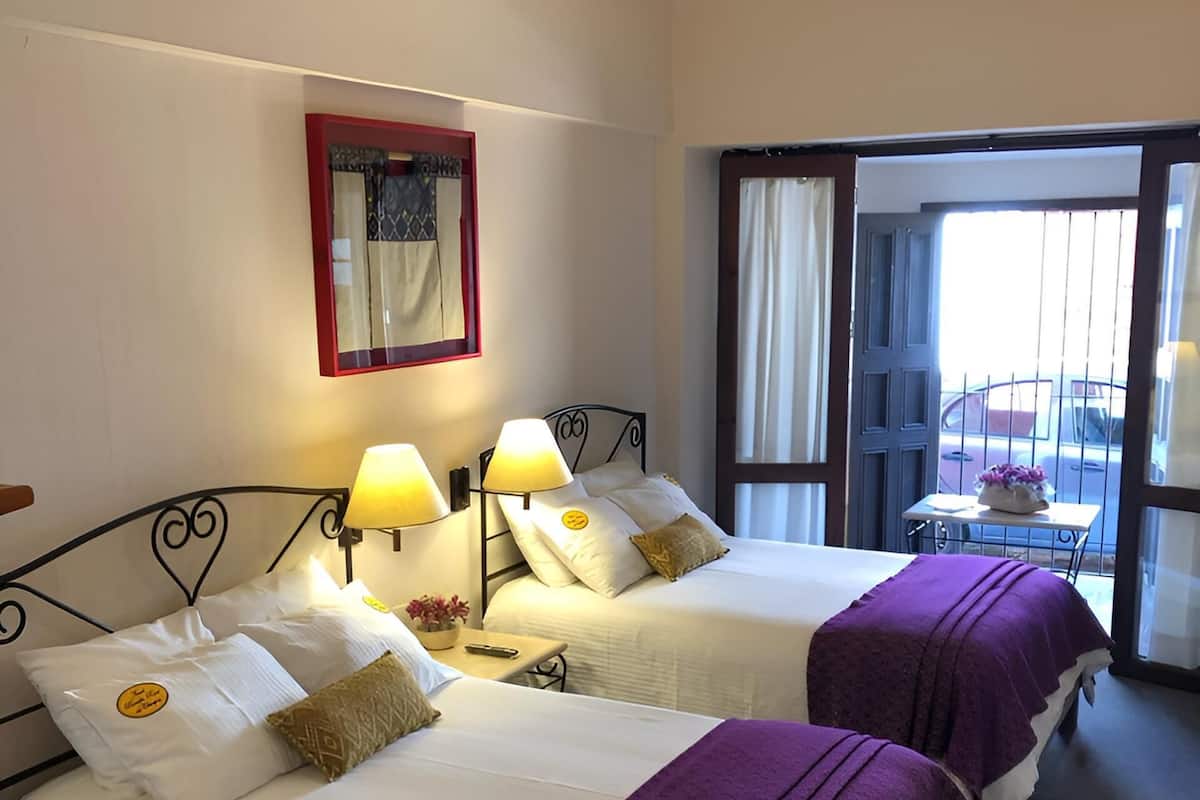 Quarto de hotel com duas camas, uma mesinha, um espelho e uma janela com vista para a rua.