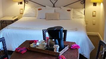 Een hotelkamer met een bed, nachtlampjes, een tafel met een koffiezetapparaat, kopjes en een dienblad.