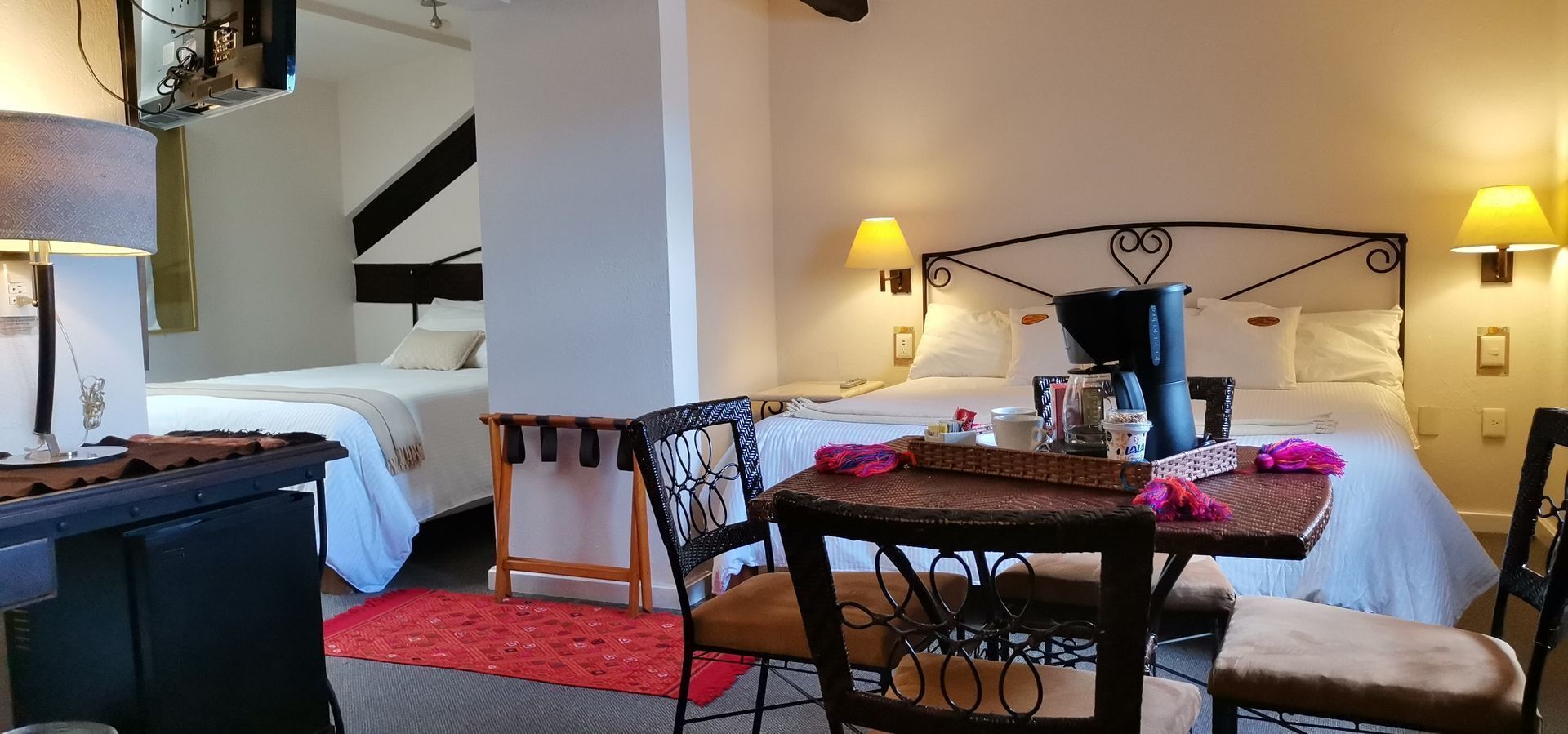 A hotel room with a bed, a desk, a chair, a table, and two wall-mounted lamps.