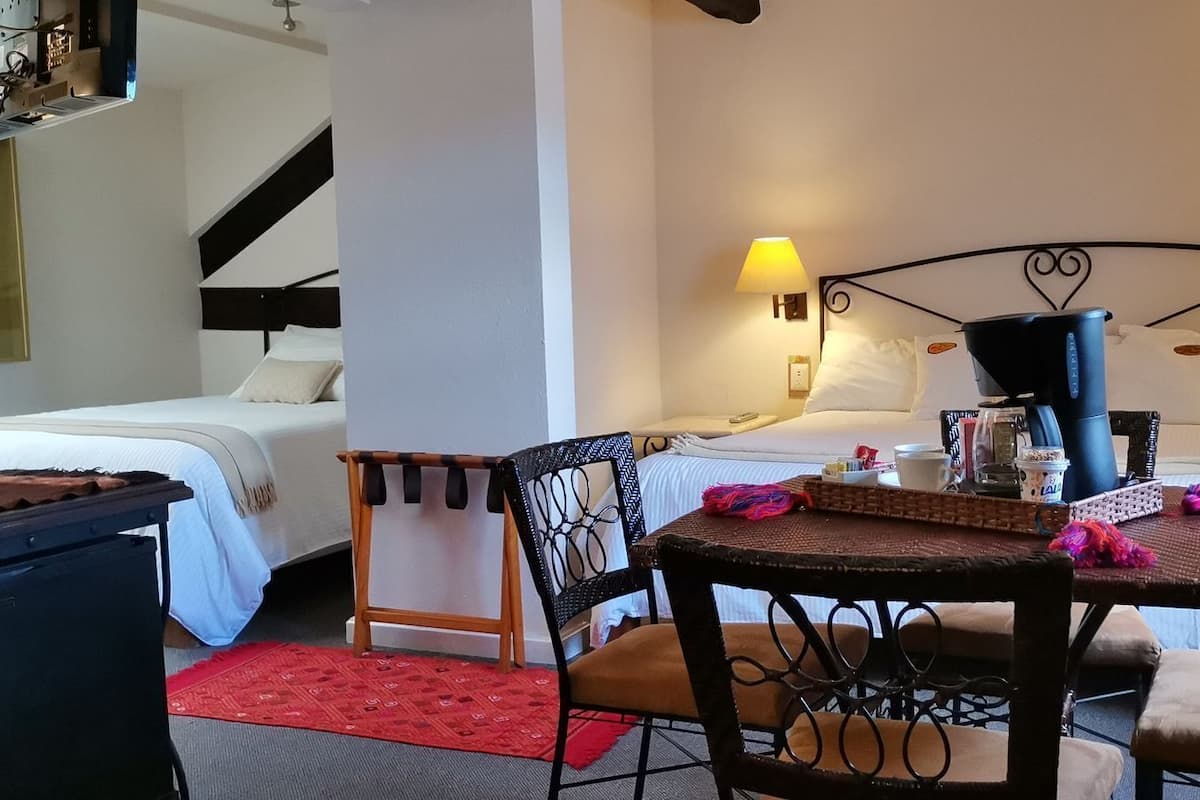 A hotel room with a bed, a desk, a chair, a table, and two wall-mounted lamps.