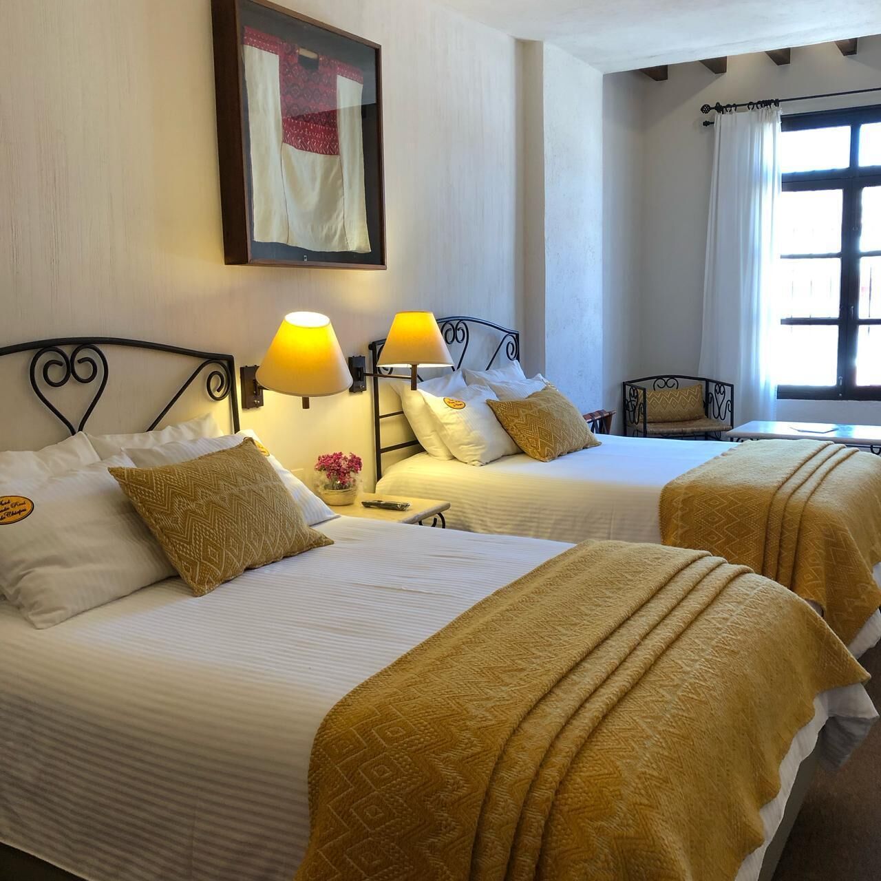 A hotel room with two beds, each with a headboard, bedside lamps, and a painting on the wall.