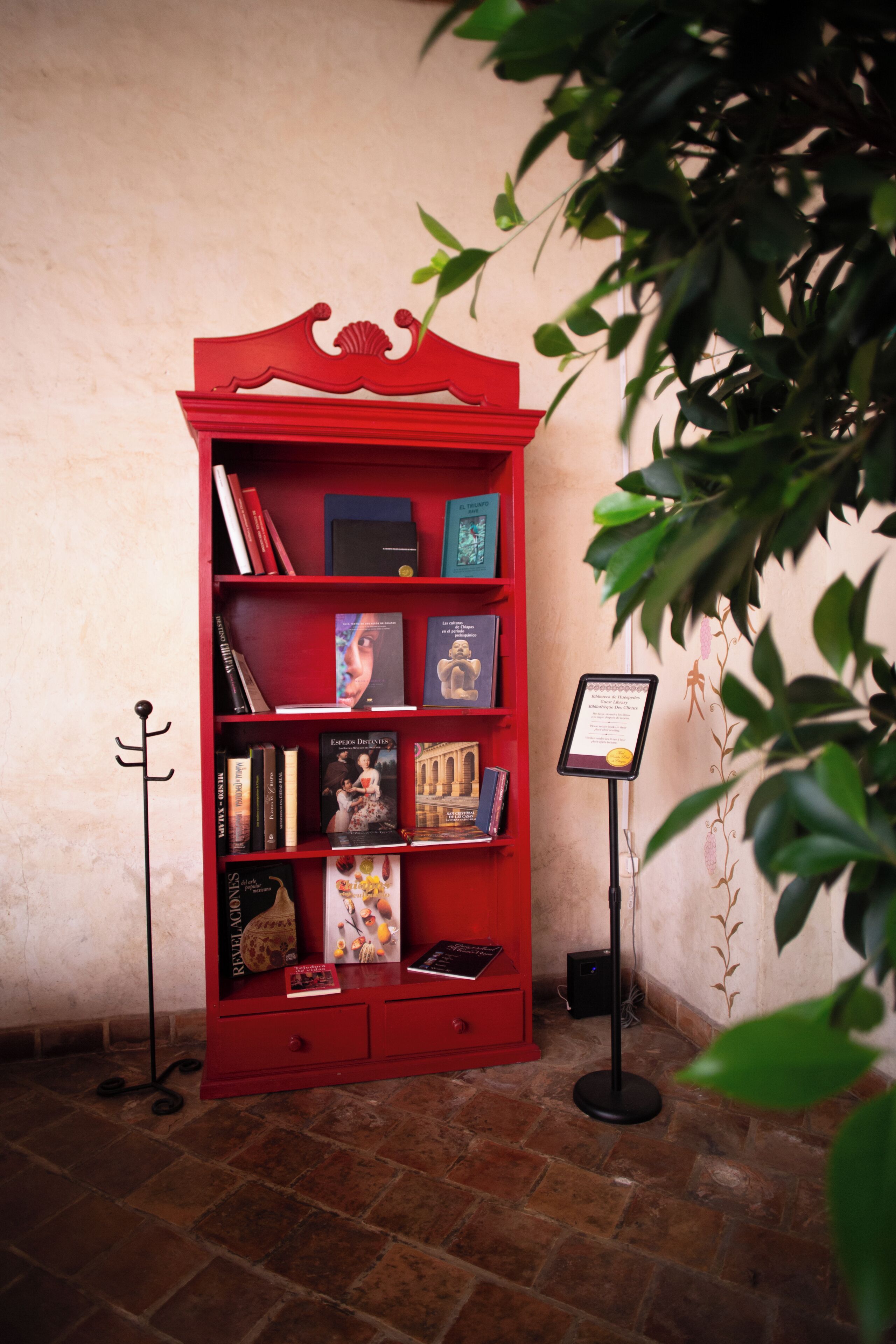 Una estantería roja con libros y un cartel, frente a una pared con una planta.
