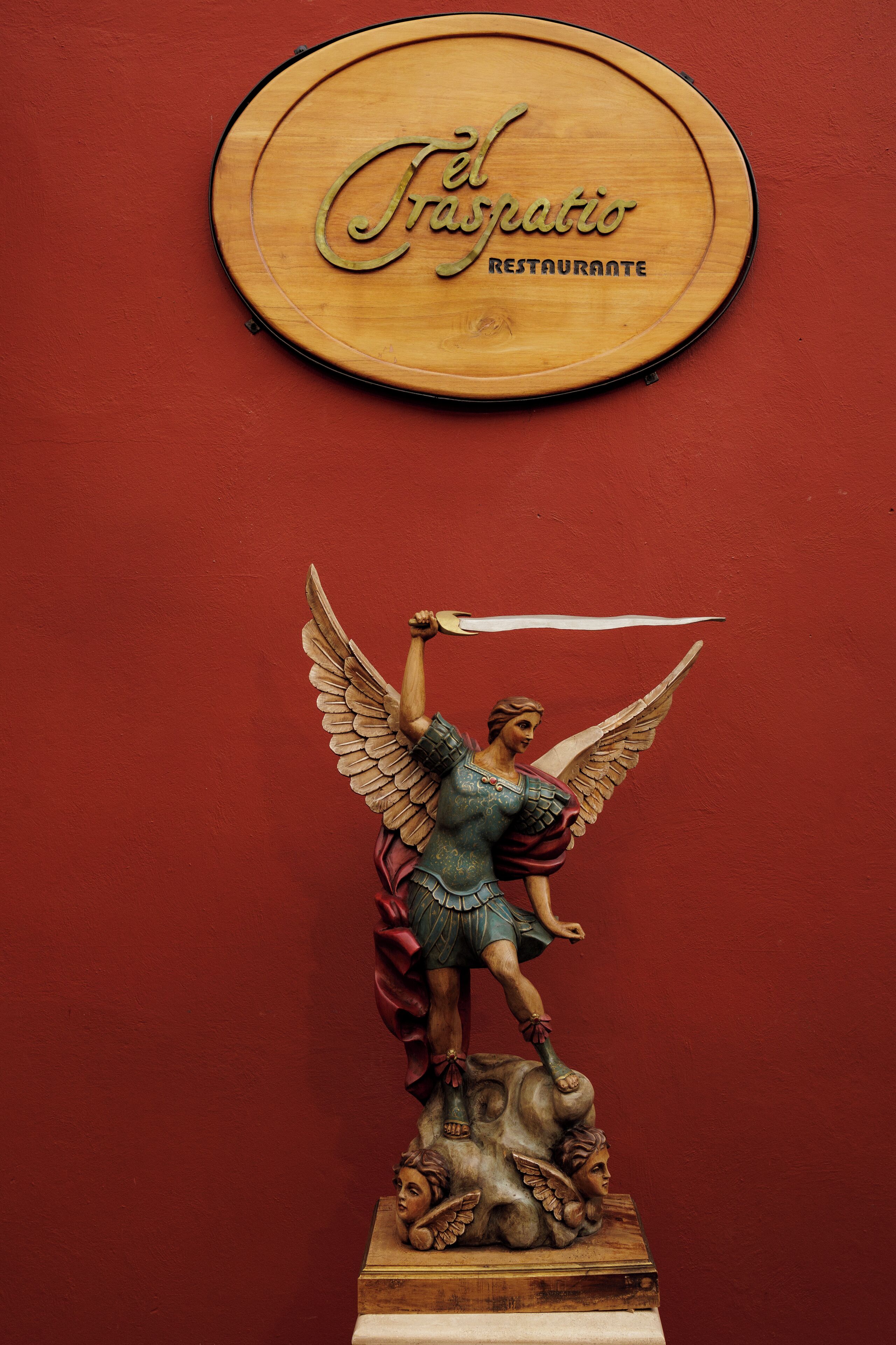 A wooden plaque with "El Fraspatio Restaurante" and a statue of an angelic figure with wings.