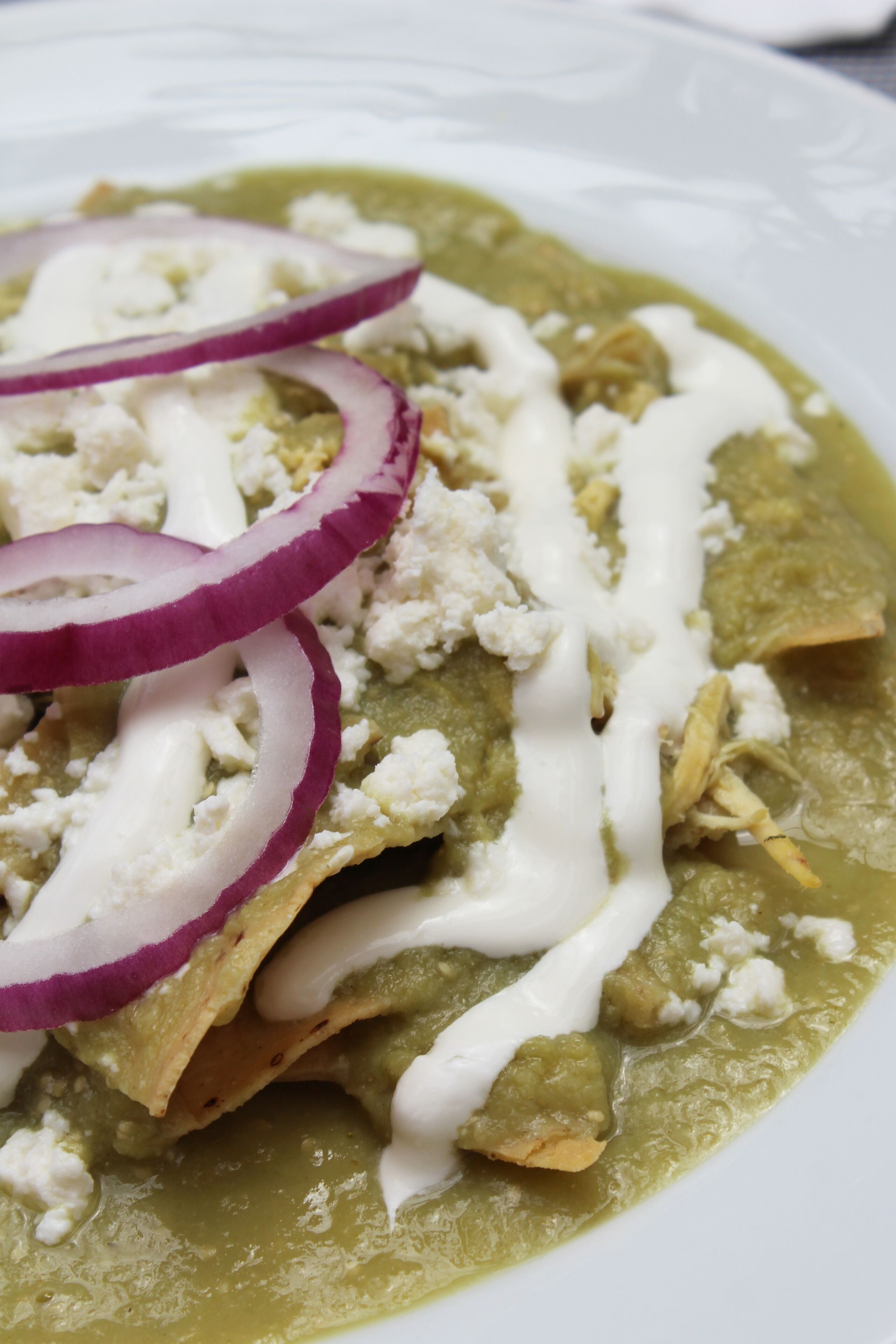 A plate of nachos topped with sour cream, crumbled cheese, and red onion slices.