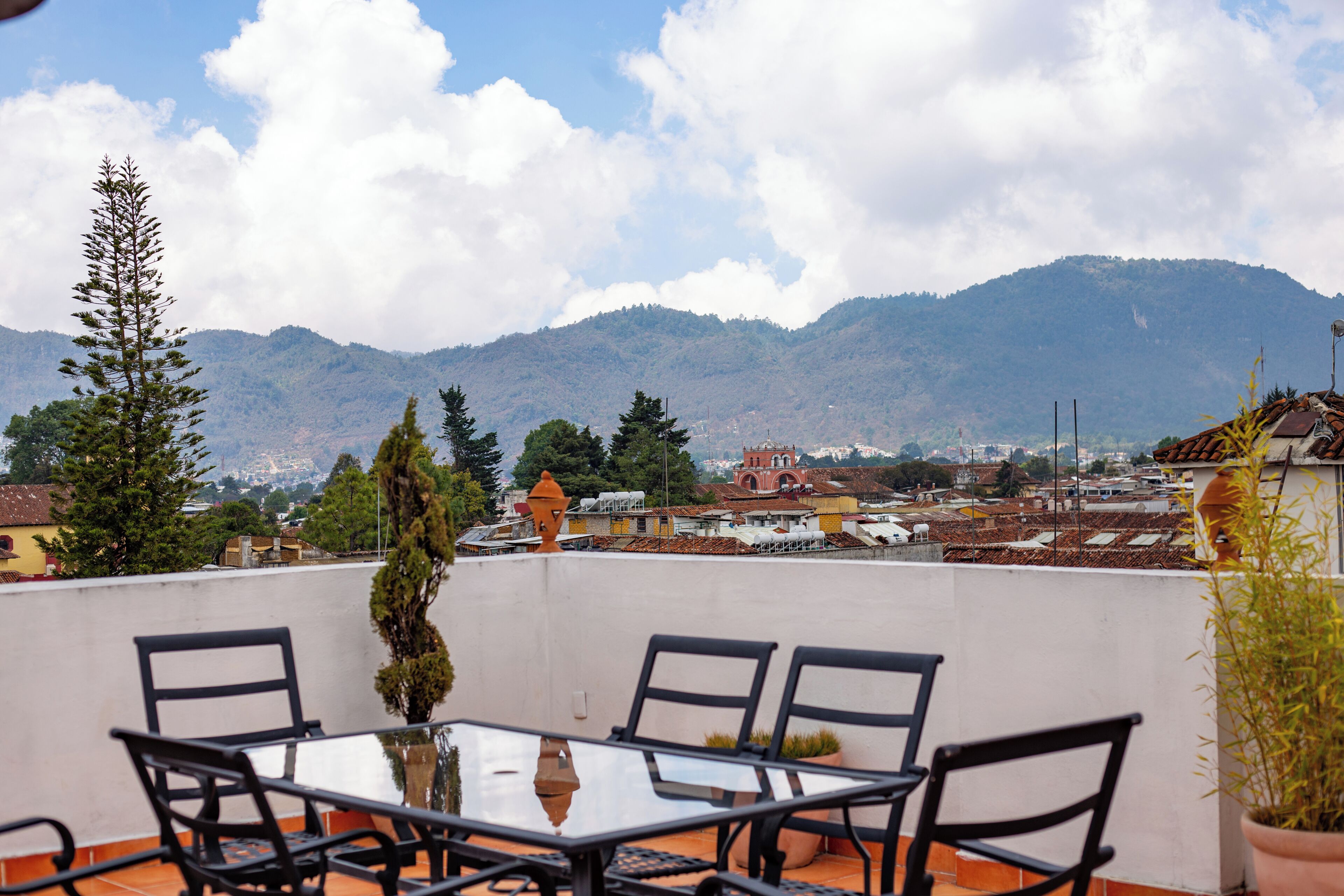 A terrace with a glass table and chairs, overlooking a cityscape with mountains in the background.