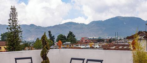 A terrace with a glass table and chairs, overlooking a cityscape with mountains in the background.