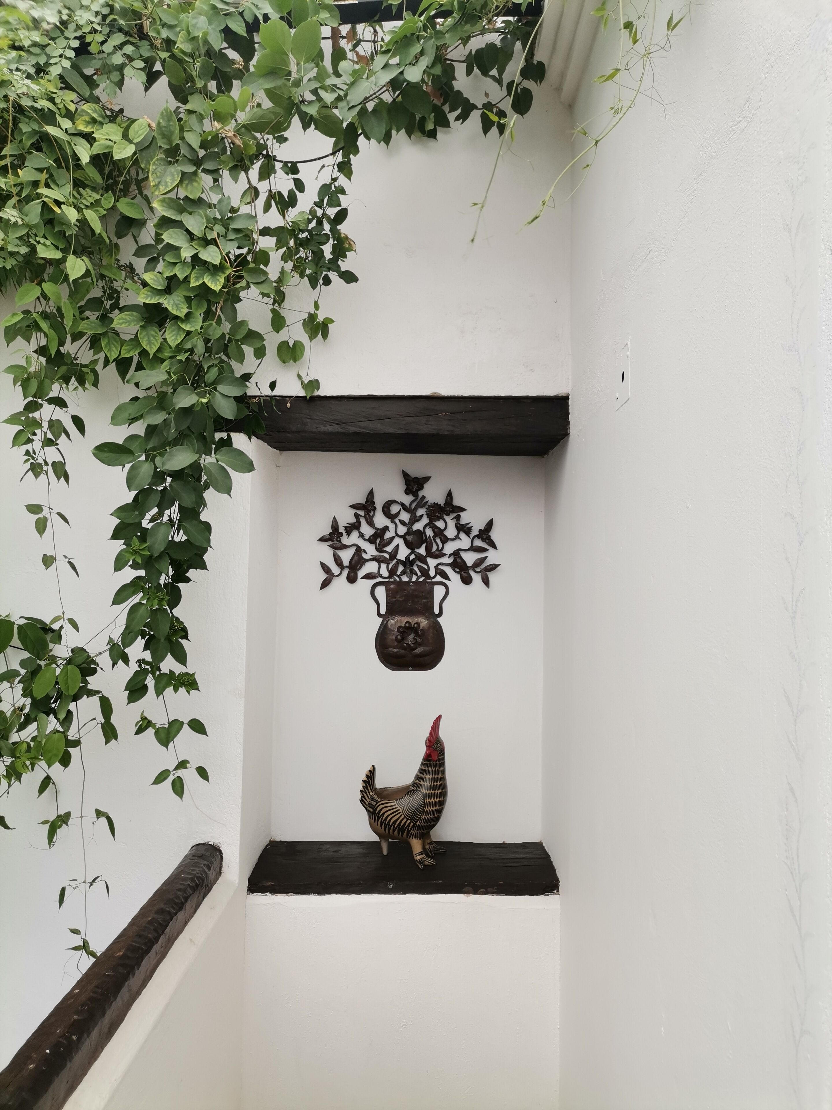 A white wall with a decorative metal pot and a rooster sculpture.
