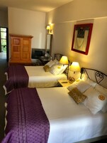 Habitación de hotel con dos camas, un armario de madera, un escritorio con lámpara y un televisor montado en la pared.