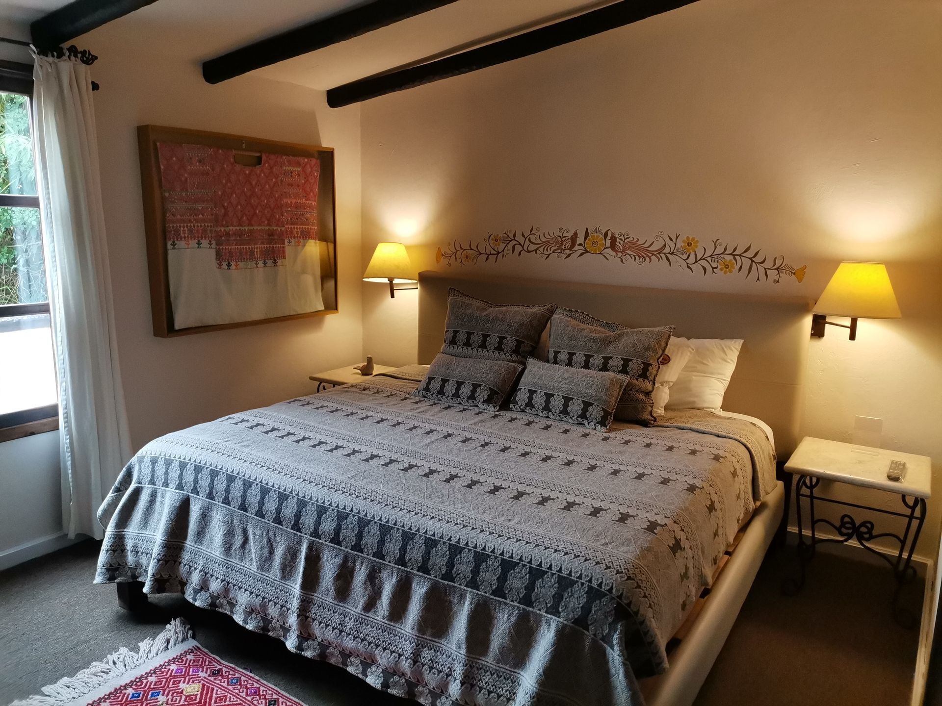 A bed with patterned bedding, two bedside lamps, a decorative wall hanging, and a window with curtains.