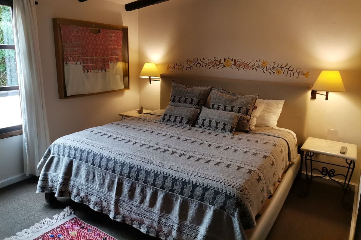A bed with patterned bedding, two bedside lamps, a decorative wall hanging, and a window with curtains.