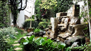 A garden with a stone water feature, lush greenery, and a statue. - Posada Real de Chiapas (San Cristóbal de las Casas)