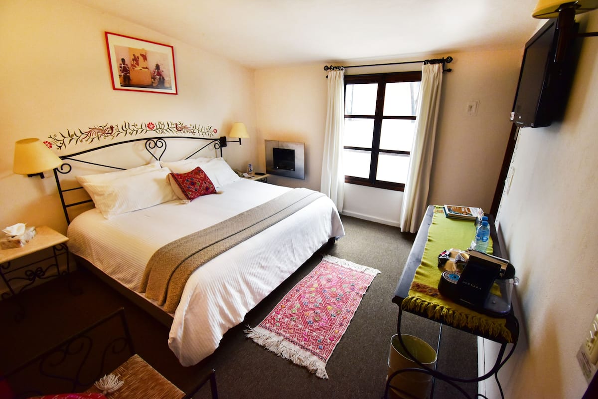 Quarto de hotel com cama, abajures, televisão, escrivaninha com computador e janela com cortinas.