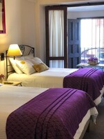 Une chambre d’hôtel avec deux lits, une table de chevet, une lampe, une fenêtre avec des rideaux et une vue sur la rue.