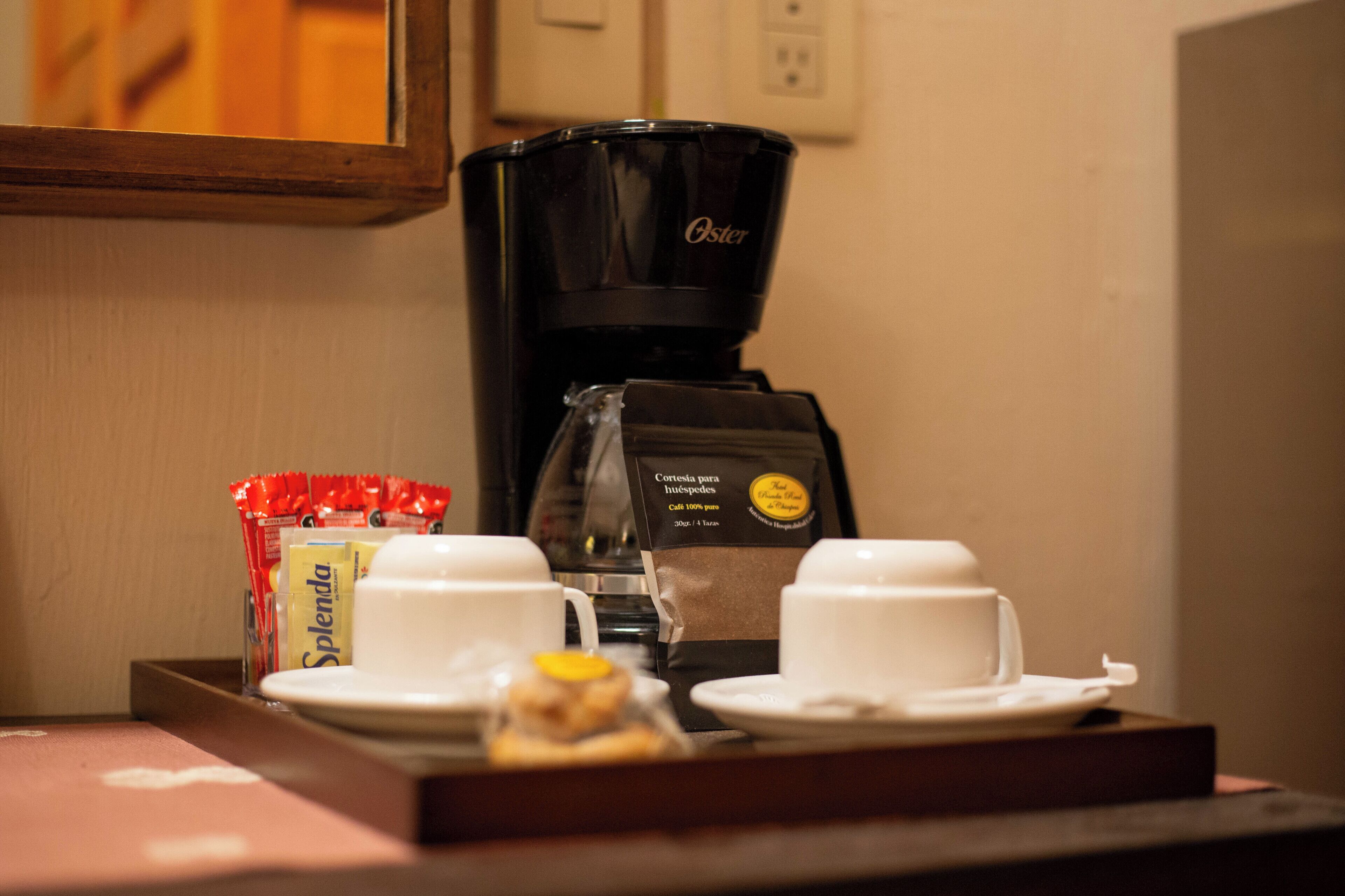 A coffee station with a coffee maker, cups, and a tray with a packet of Splenda and a small pastry.