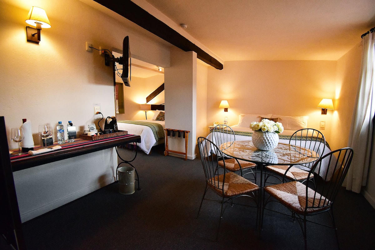 Quarto de hotel com área de jantar, cama e escada.
