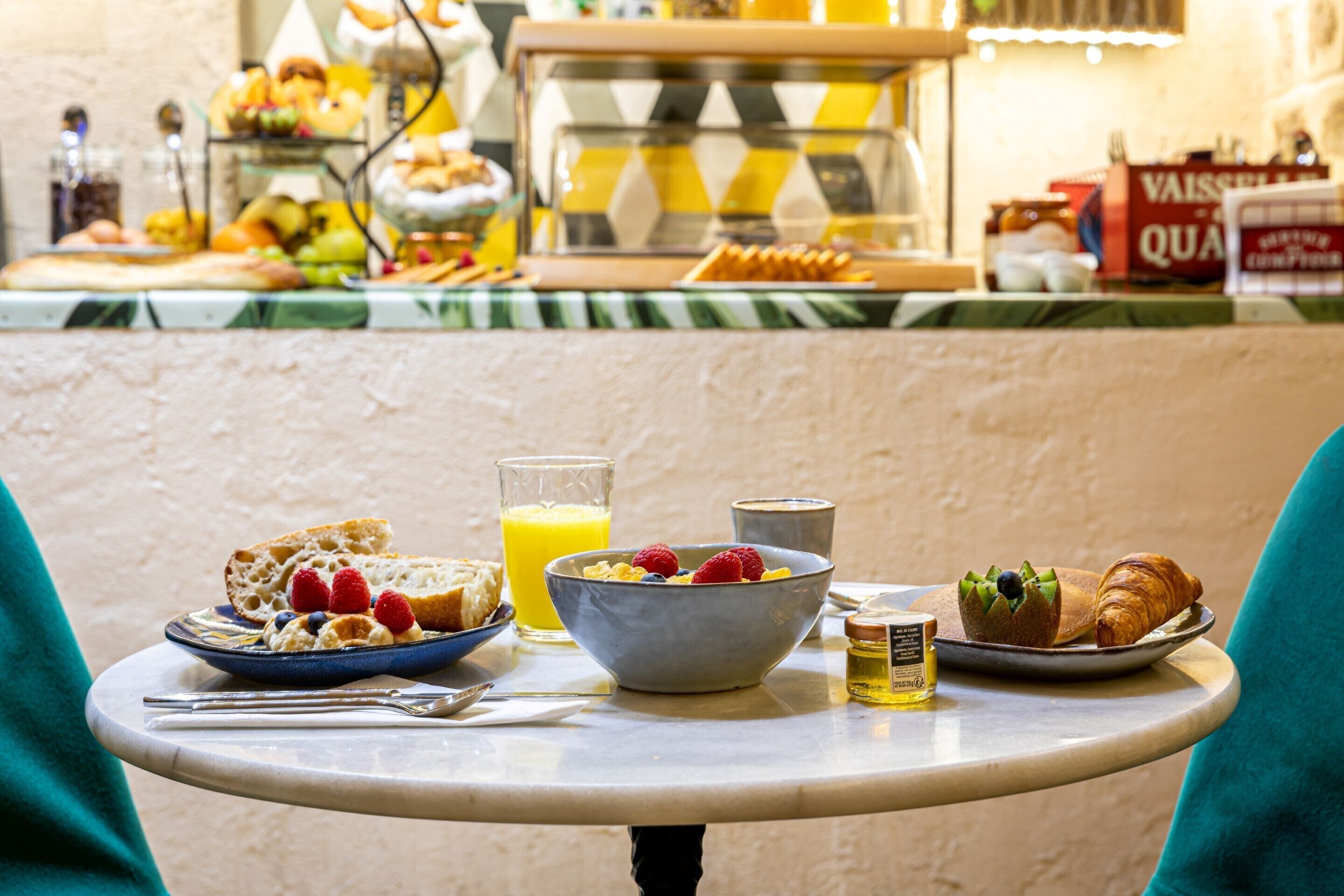 Ein Esstisch mit einer Schüssel Müsli, einem Croissant, einem Glas Orangensaft und einer Auswahl an Gebäck.