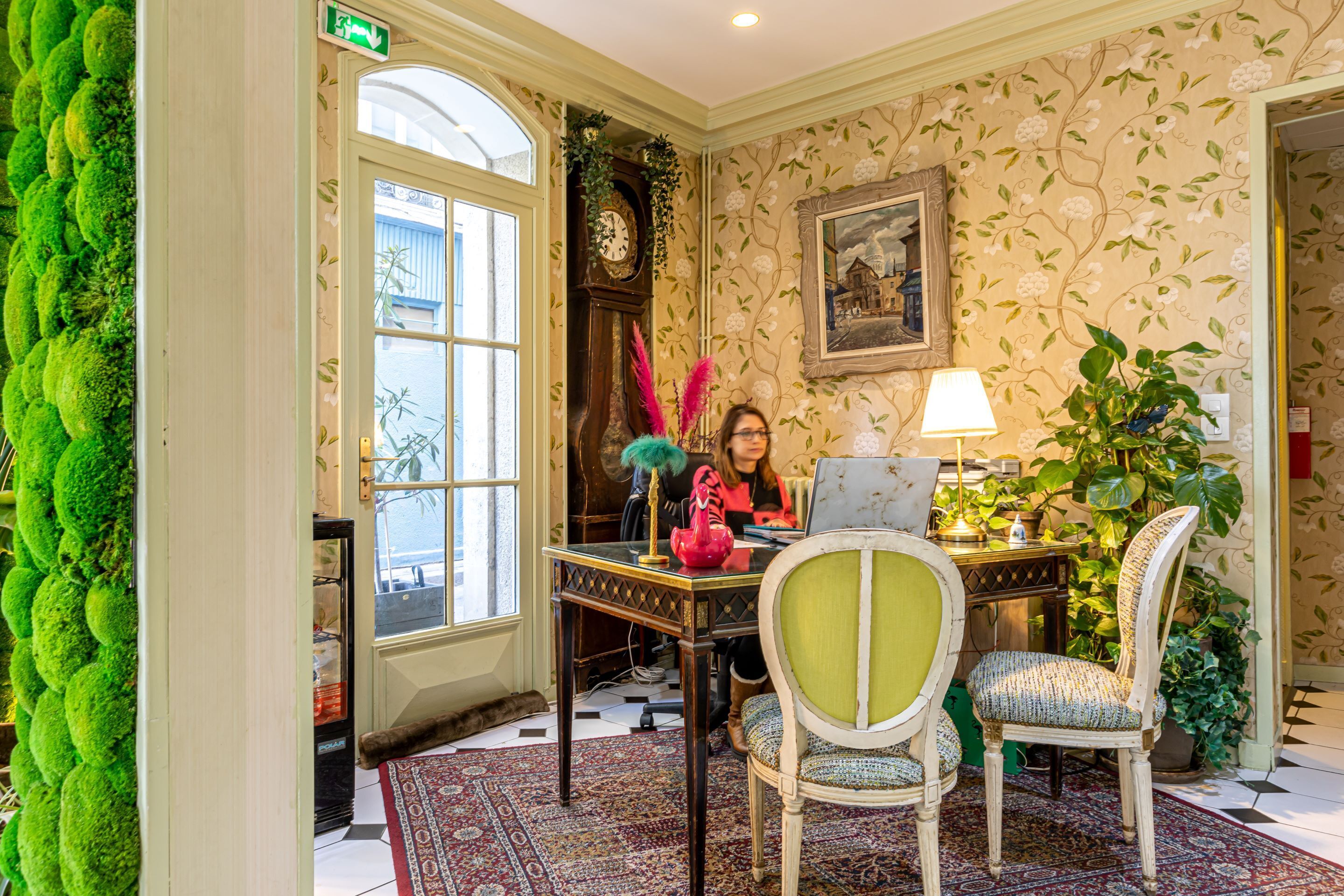 A room with a large window, a clock, a table with chairs, and a plant.