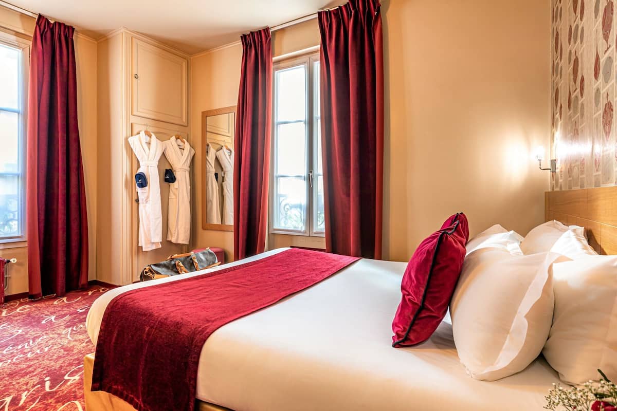 Una habitación de hotel con una cama grande, cortinas rojas, batas blancas y un plaid rojo.