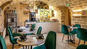 Un restaurante rústico con paredes de piedra, sillas tapizadas de verde, una barra y una cocina visible al fondo.