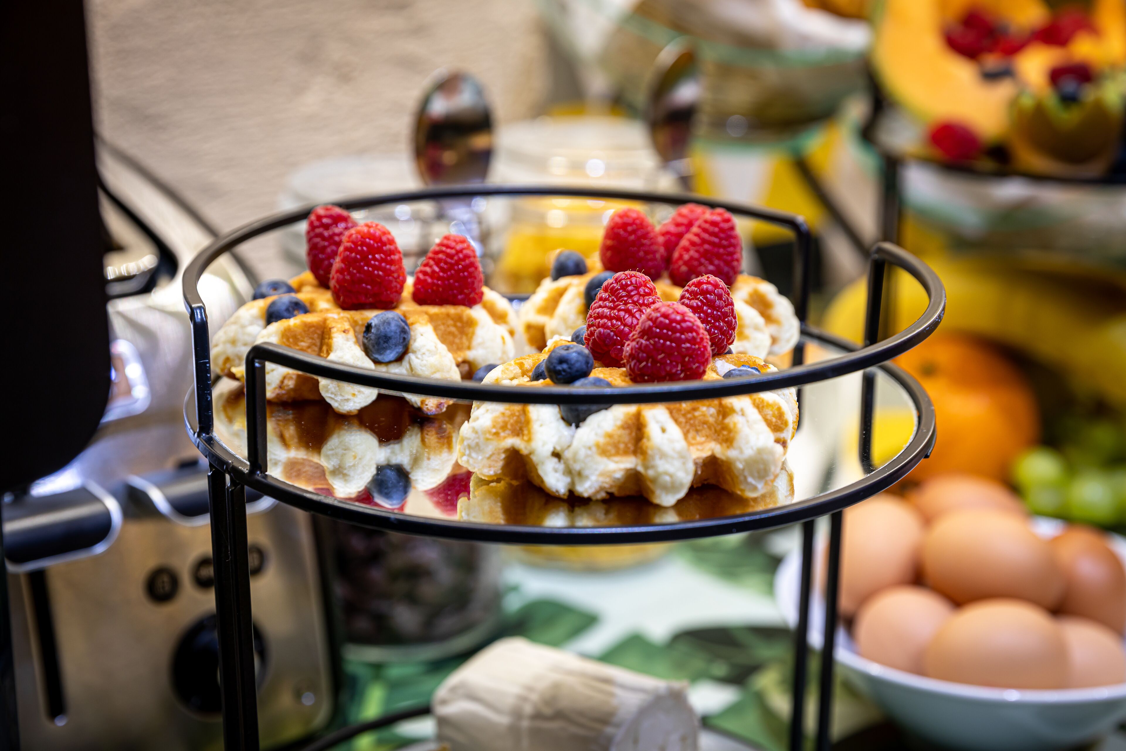 Un bufé de desayuno con waffles cubiertos de bayas y un bol de huevos.