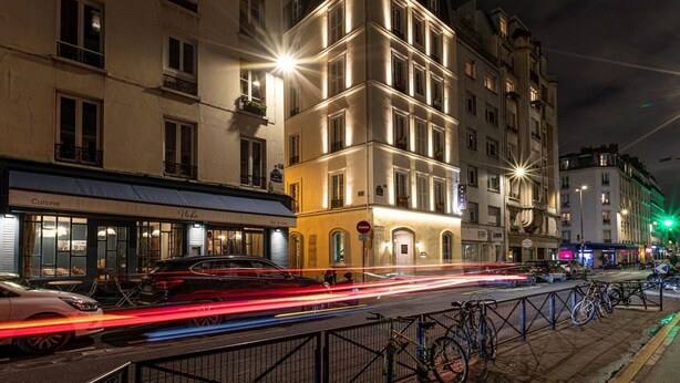 Una escena nocturna en la calle con edificios iluminados, un restaurante llamado 'Roche' y bicicletas estacionadas a lo largo de la acera.