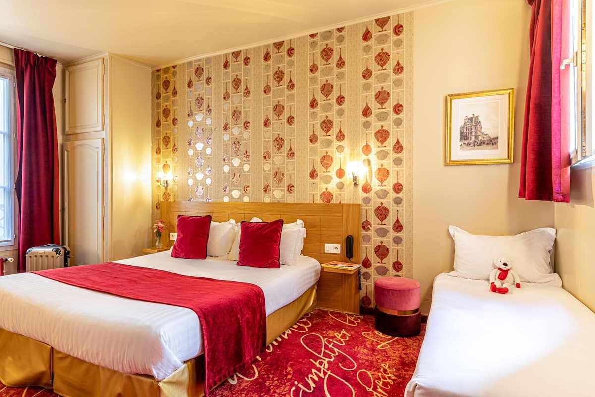 Una habitación de hotel con dos camas, alfombra roja y un papel tapiz estampado.