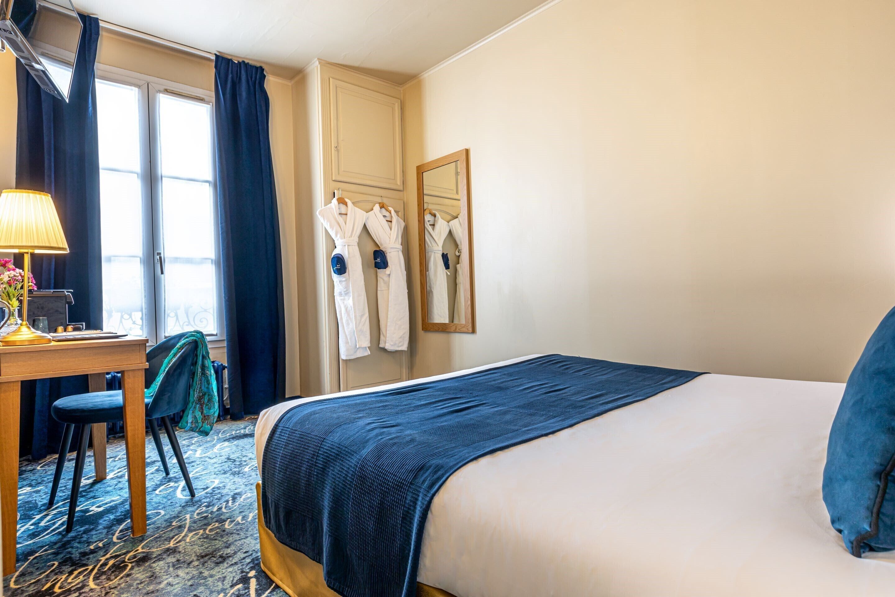 Habitación de hotel con cama, escritorio, silla, lámpara y ventana con cortinas.