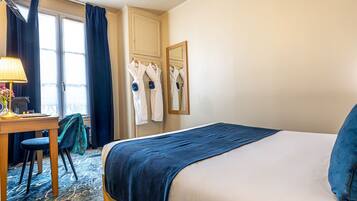 Habitación de hotel con cama, escritorio, silla, lámpara y ventana con cortinas.