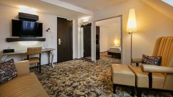 A hotel room with a flat-screen TV, a desk, a bed, a sofa, and a chair.