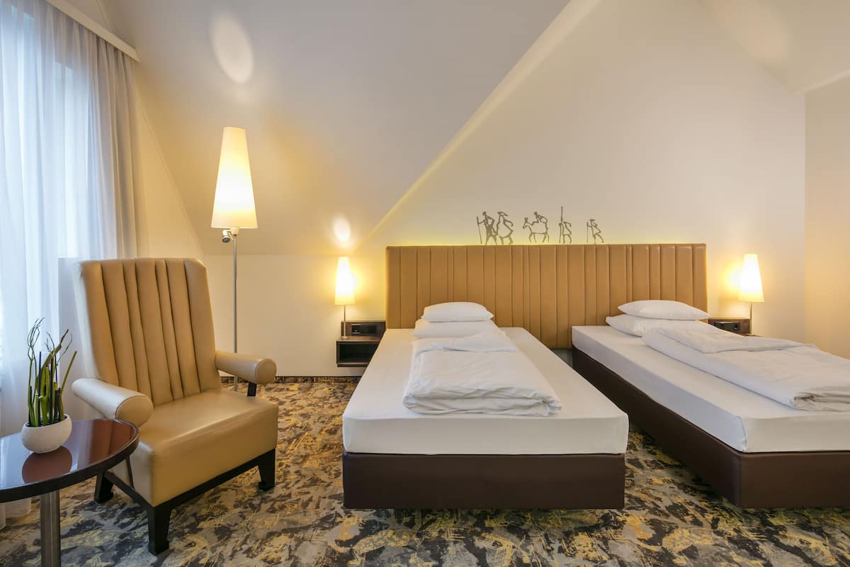 Quarto de hotel com duas camas, uma cadeira, uma mesa com uma planta e duas luminárias de parede.