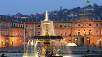 Ein historisches Gebäude mit einem zentralen Brunnen, einem gepflegten Garten und einer Statue im Vordergrund.