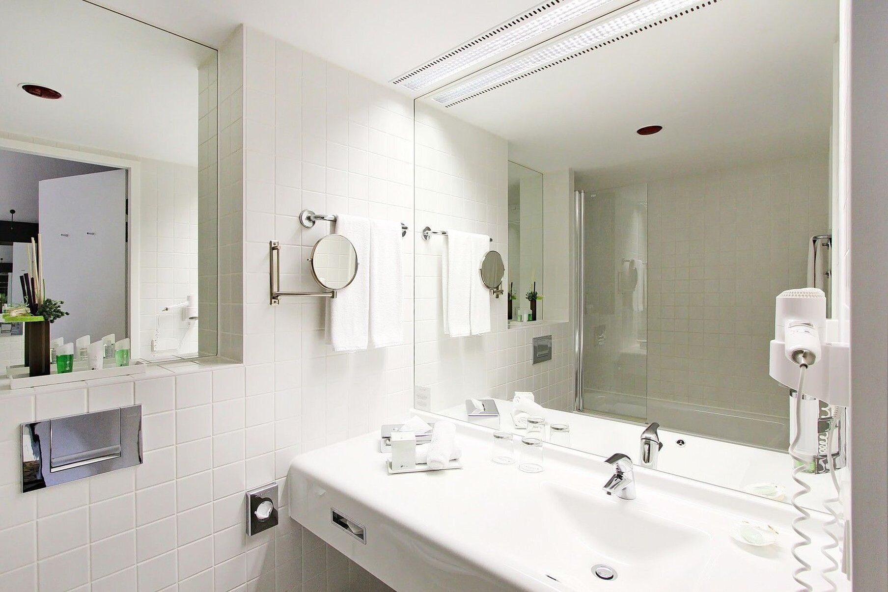 Une salle de bain moderne avec un lavabo blanc, deux miroirs, un porte-serviettes et un sèche-cheveux.