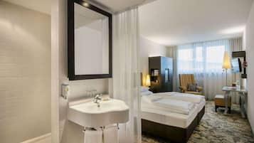 A hotel room with a large bed, a bathroom with a sink and mirror, a desk with a chair, and a TV.