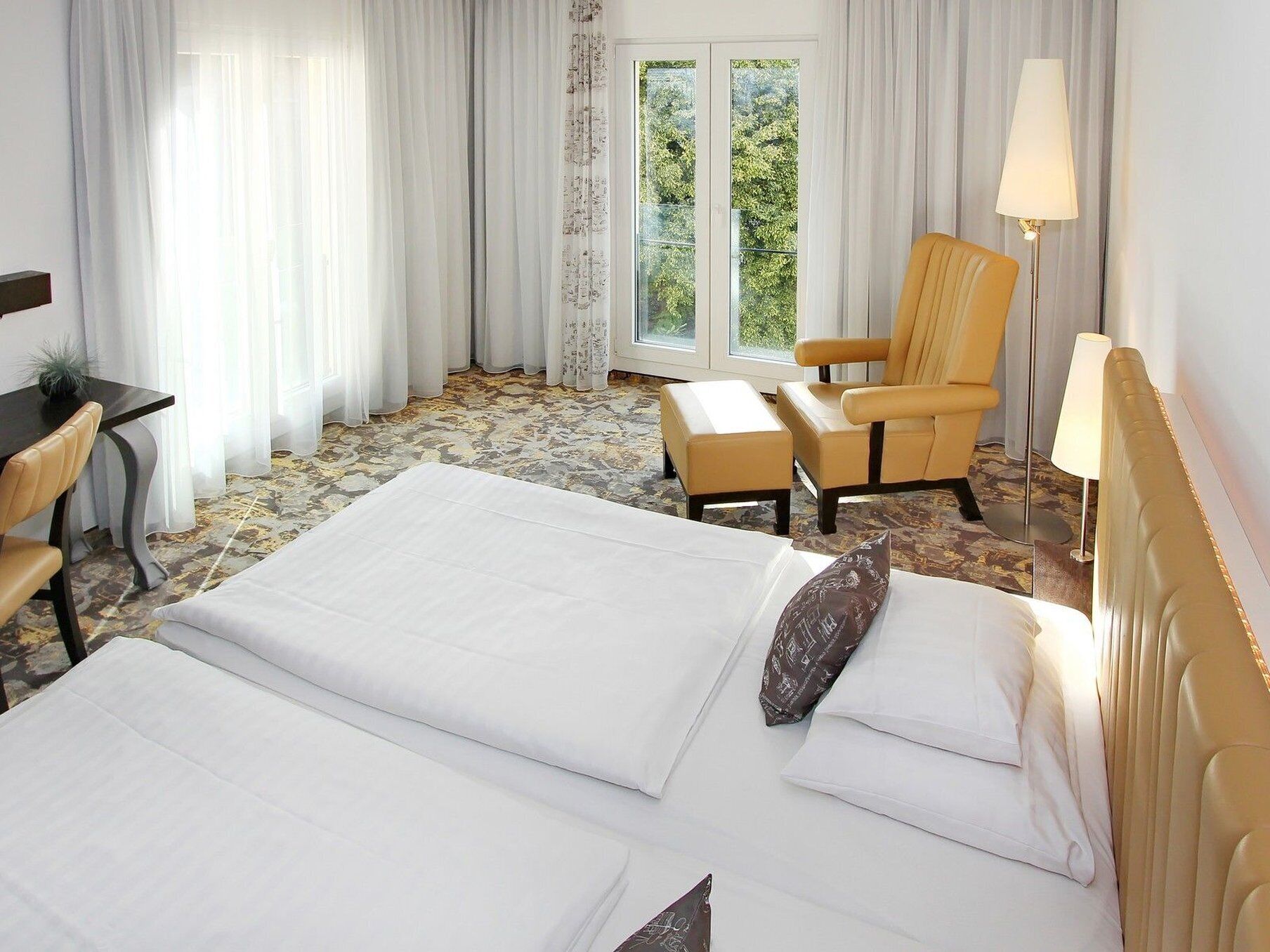 A hotel room with a bed, a chair, a desk, and a lamp.