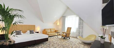 A modern hotel room with a large bed, a sofa, a chair, and a TV.