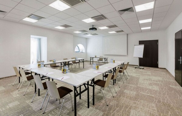 A conference room with a long table, chairs, a projector, a whiteboard, and a door.