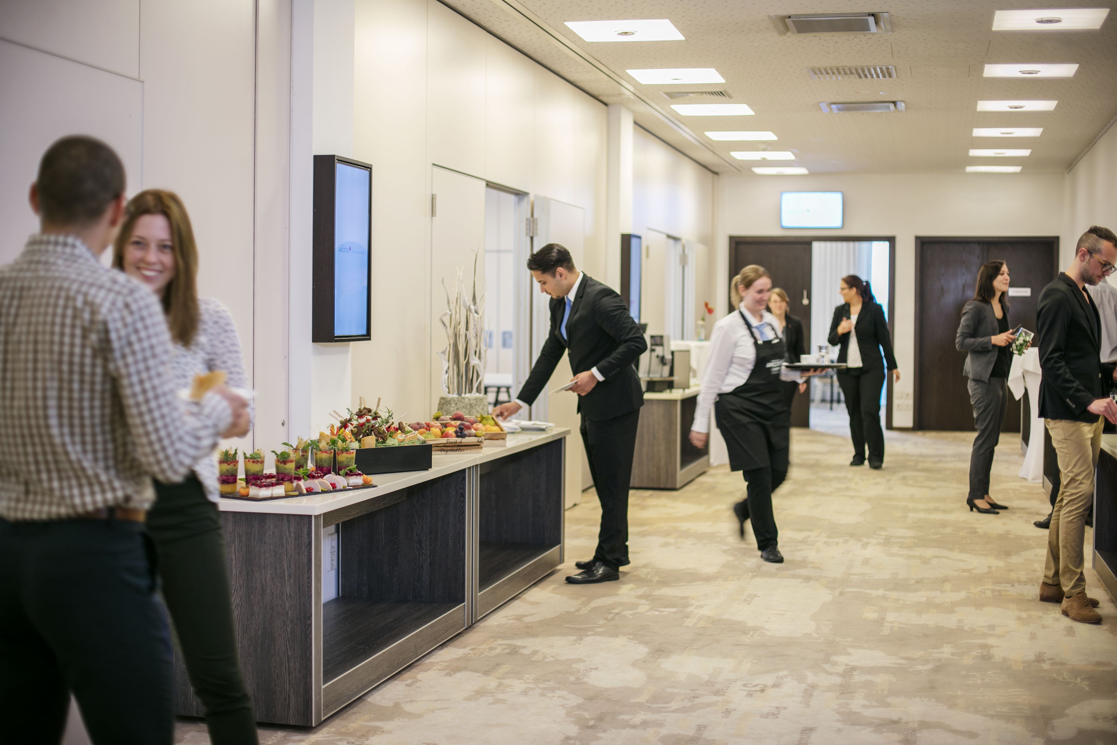 A modern hotel lobby with a reception desk, a buffet area, and a spacious layout.