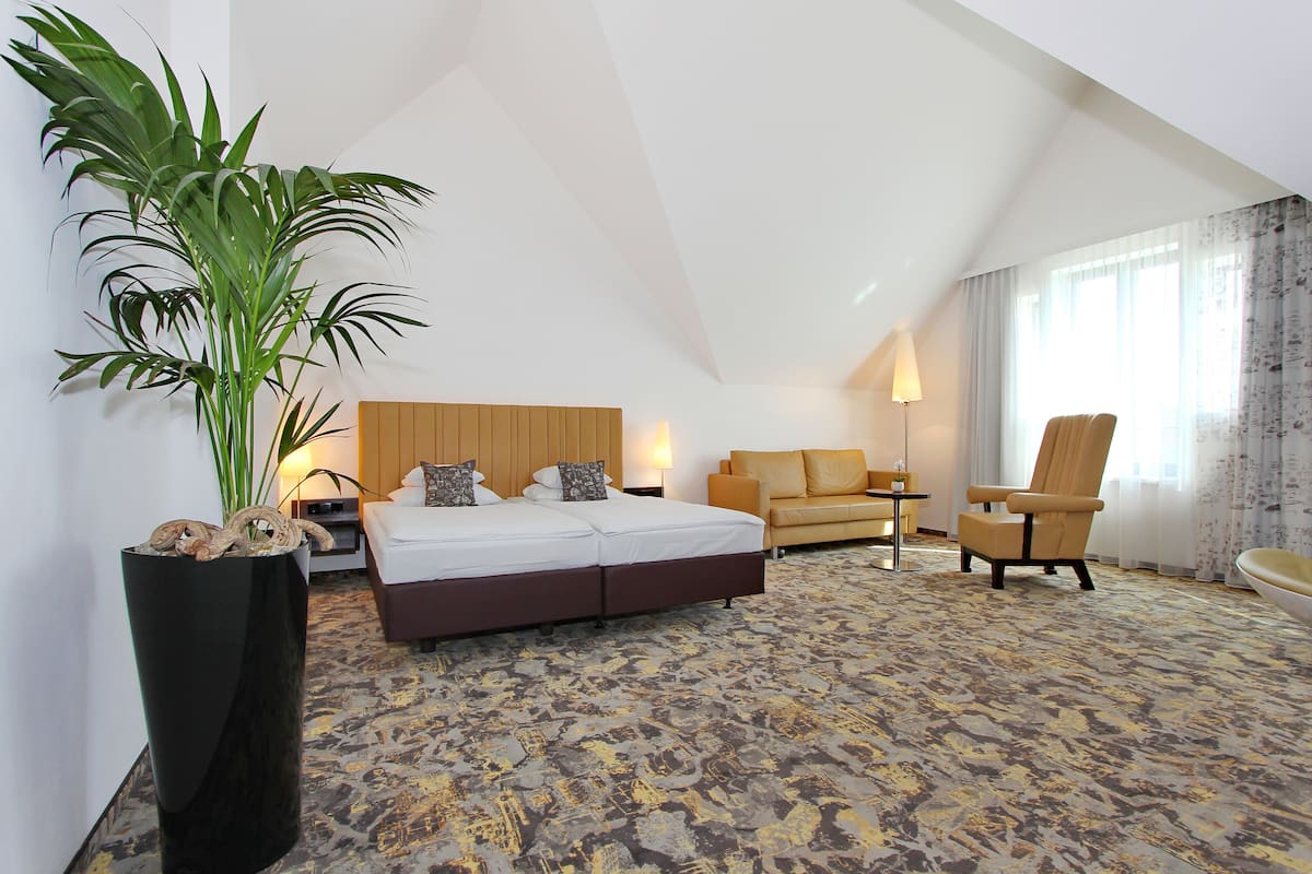 Quarto de hotel com uma cama grande, um sofá, uma cadeira e um vaso de planta.