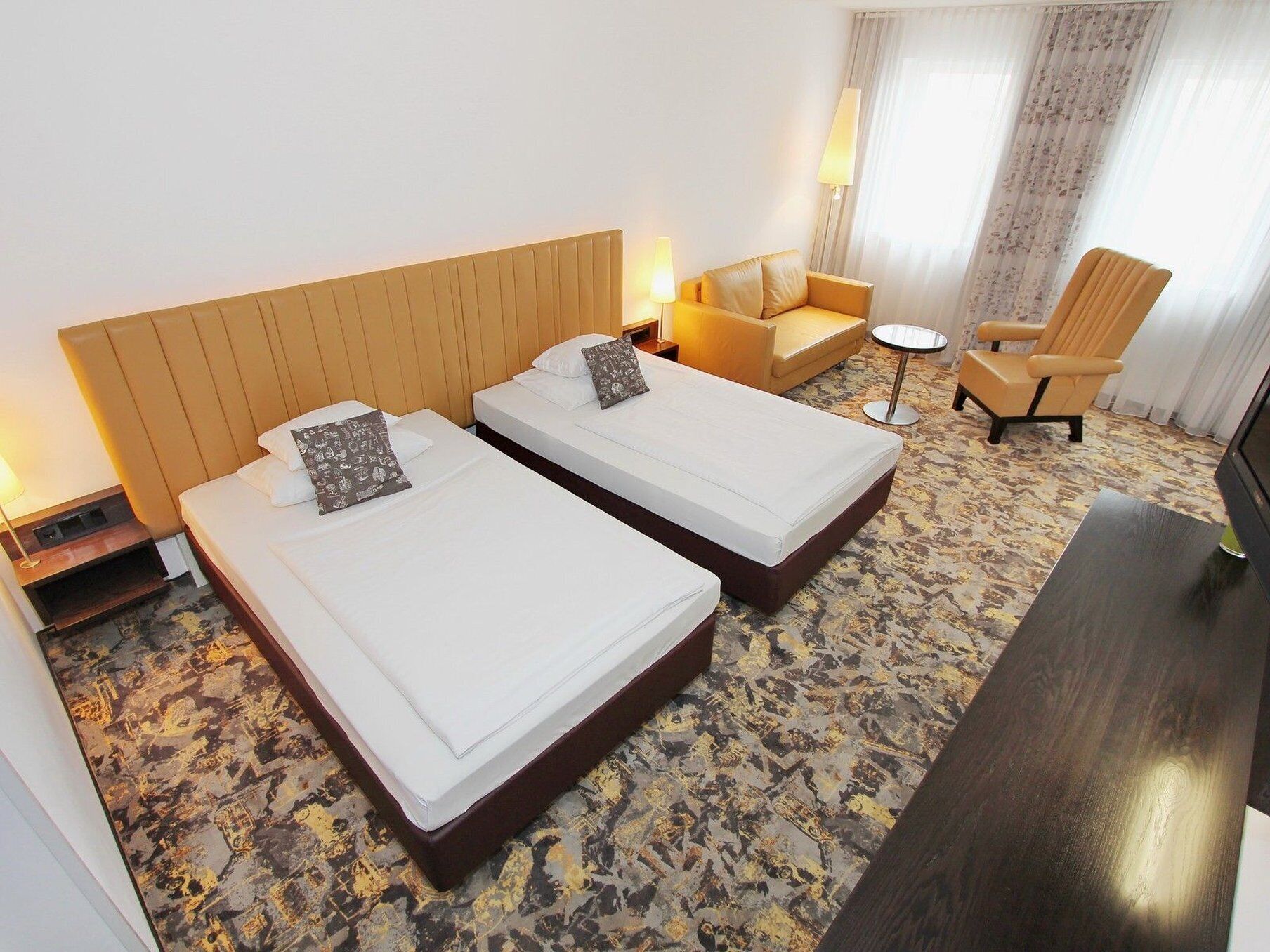 Habitación de hotel con dos camas, un sofá, una silla, una mesita y un televisor.