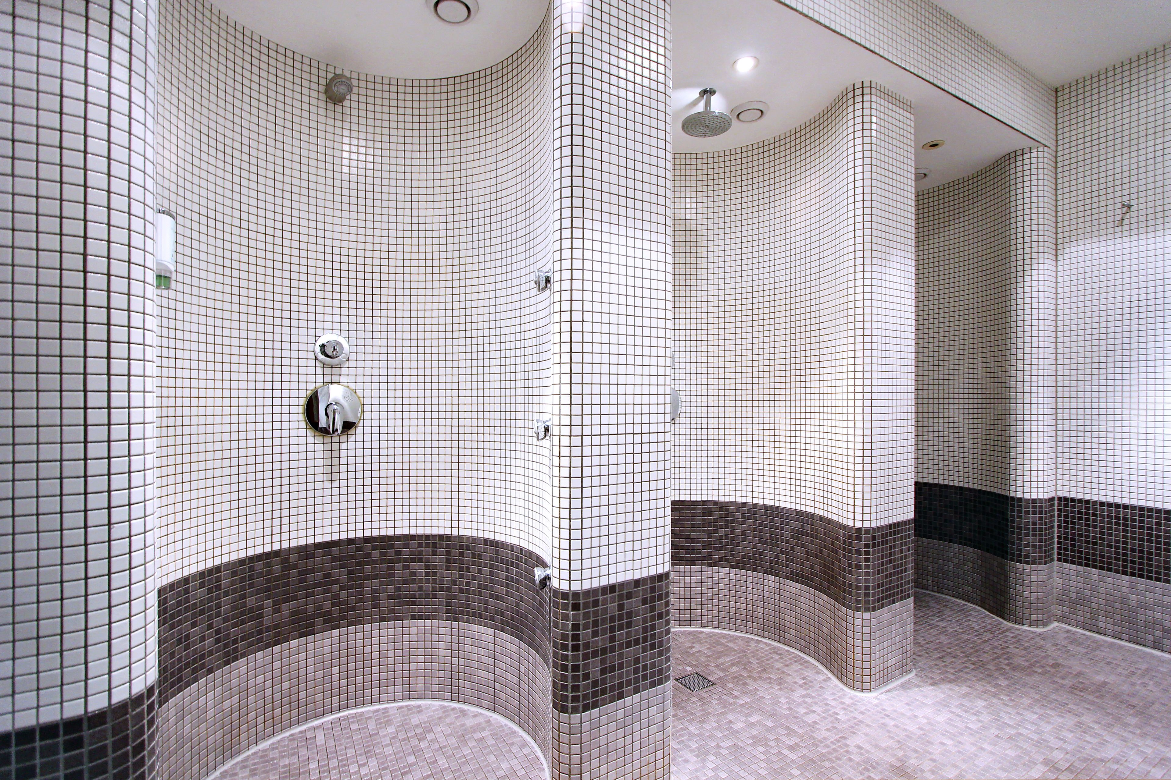 A bathroom with white and brown tiled walls, a shower area, and a mirror.