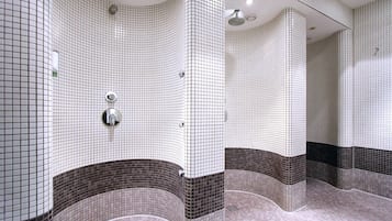 A bathroom with white and brown tiled walls, a shower area, and a mirror.