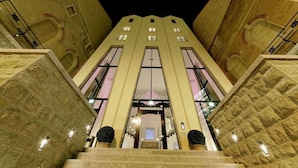 L’entrée d’un hôtel, avec un grand escalier, de grandes fenêtres et des murs en pierre.